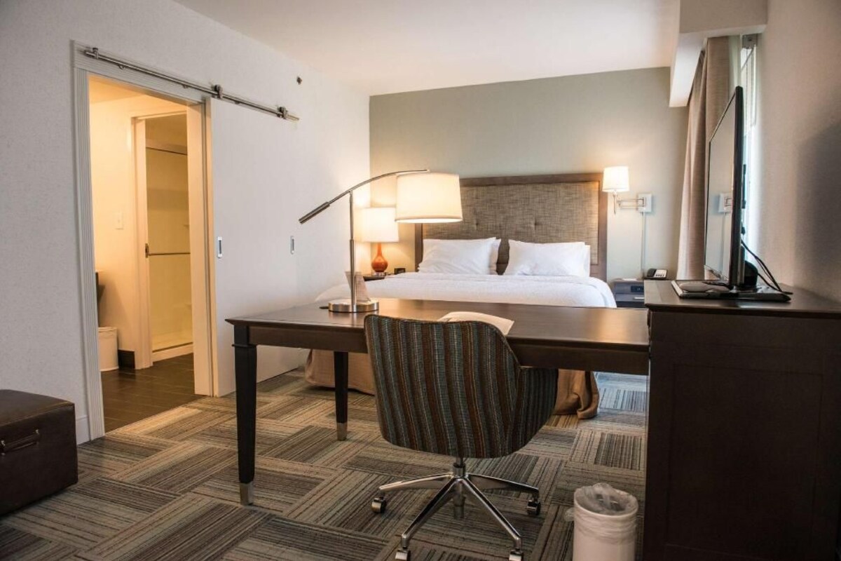 Una habitación de hotel con cama, escritorio, silla, lámpara y televisión.