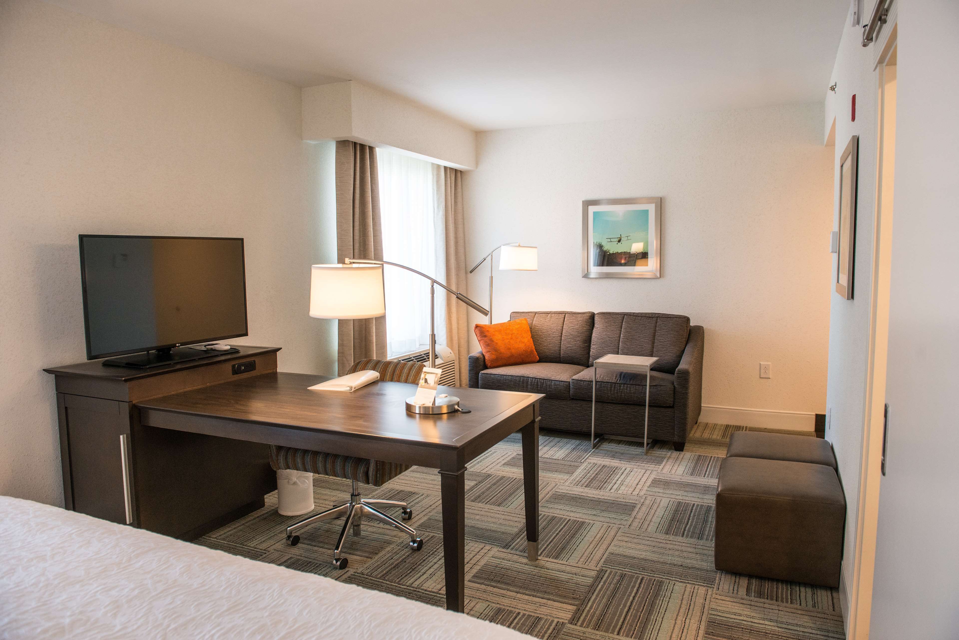 A hotel room with a bed, a desk with a television, a sofa, a lamp, and a painting on the wall.