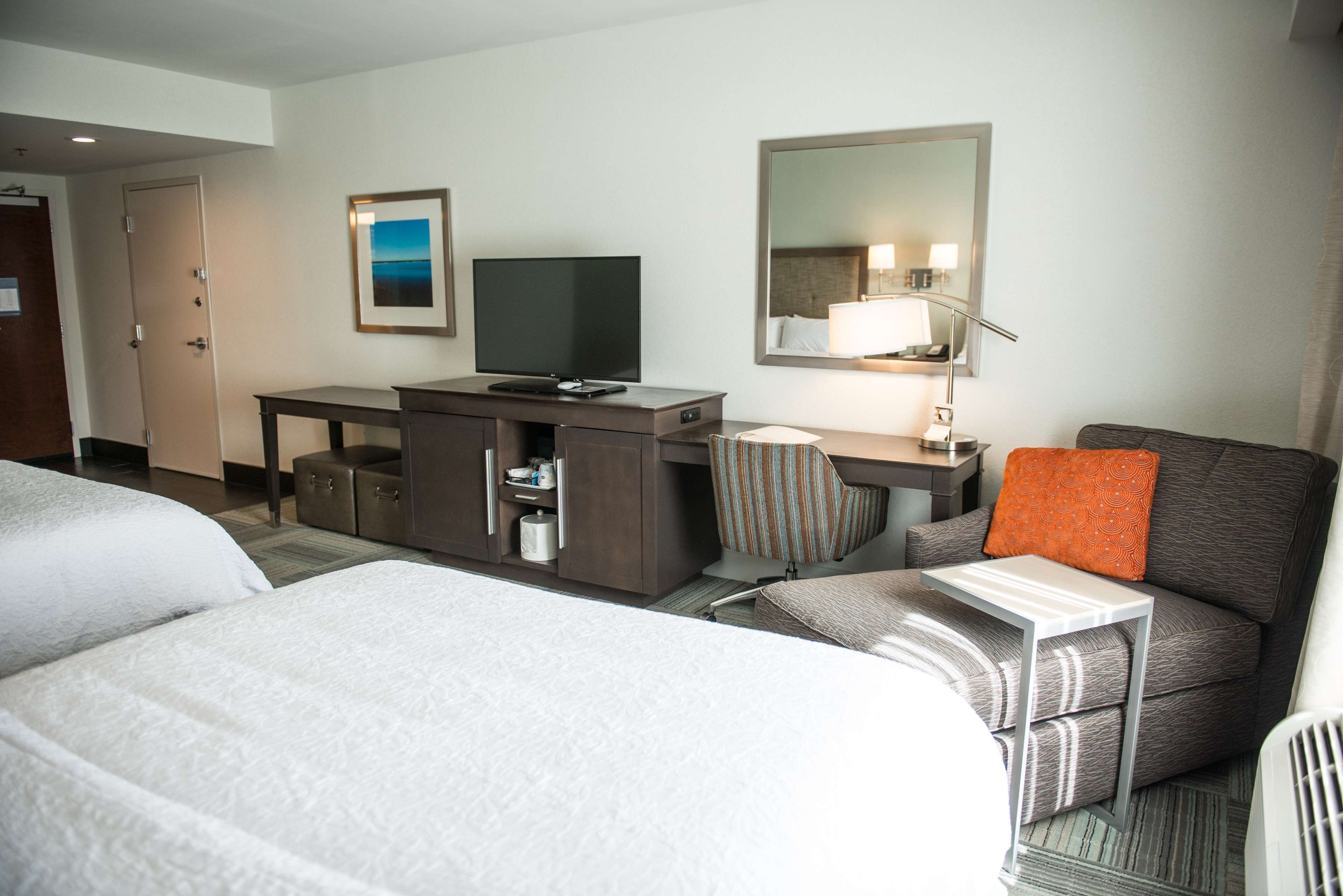 A hotel room with two beds, a desk with a television, a mirror, and a lamp.