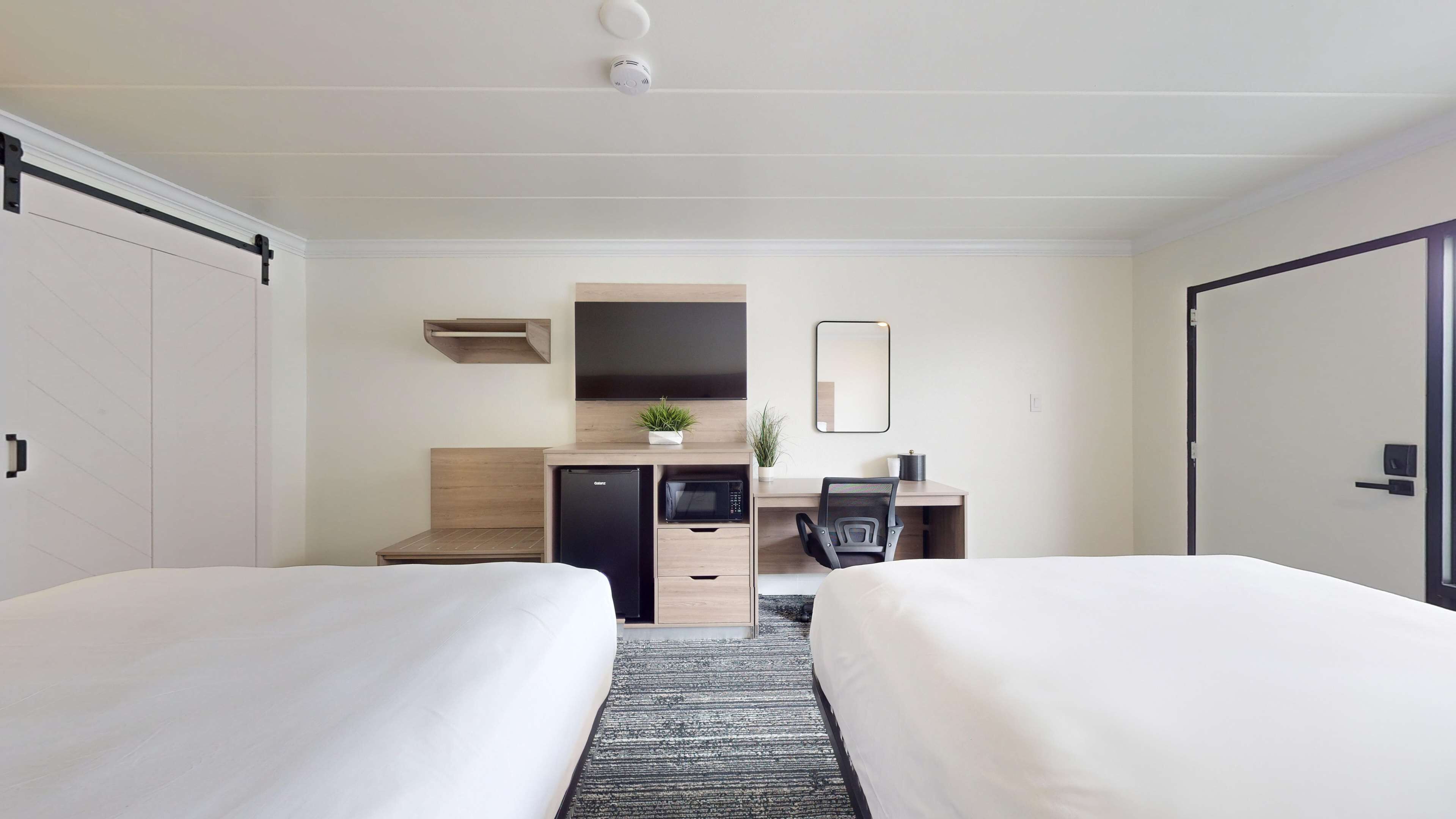 A hotel room with two beds, a desk with a computer, a microwave, and a small refrigerator.