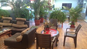 A lounge area with sofas, chairs, and a dining table with a red tablecloth. There are potted plants and a brick floor. - MundialCity Hotel Guayaquil (Guayaquil)