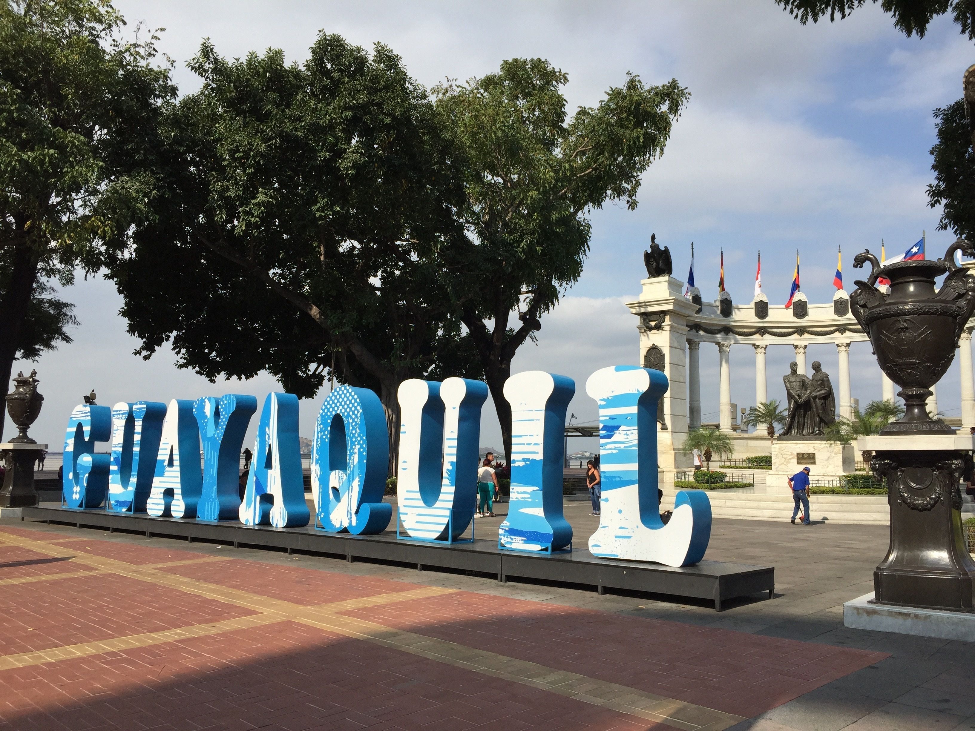A large outdoor sign with the word "HAYQUIL" in blue letters, surrounded by trees and a statue in the background.