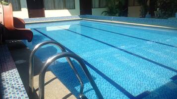 Una piscina con azulejos azules cristalinos, una escalera de metal y una zona de terraza con baldosas.