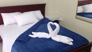 A neatly made bed with white and blue bedding, a heart-shaped towel arrangement, and a framed artwork on the wall. - MundialCity Hotel Guayaquil (Guayaquil)