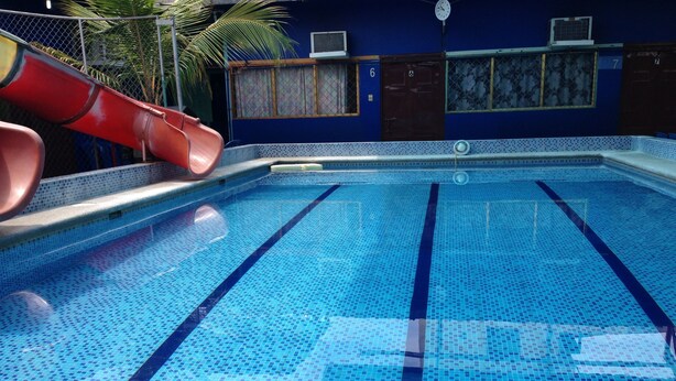 A swimming pool with clear blue tiles and lane dividers, a red slide, and a blue wall with numbered doors. - MundialCity Hotel Guayaquil (Guayaquil)