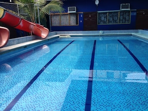A swimming pool with clear blue tiles and lane dividers, a red slide, and a blue wall with numbered doors. - MundialCity Hotel Guayaquil (Guayaquil)
