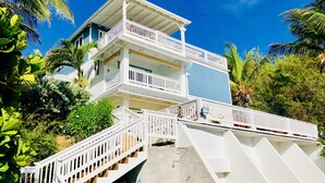 A multi-story building with white railings and a blue facade, surrounded by lush greenery. - White Caps (Bathsheba)