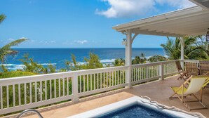 A pool area with a view of the ocean, wooden chairs, and a white railing. - White Caps (Bathsheba)