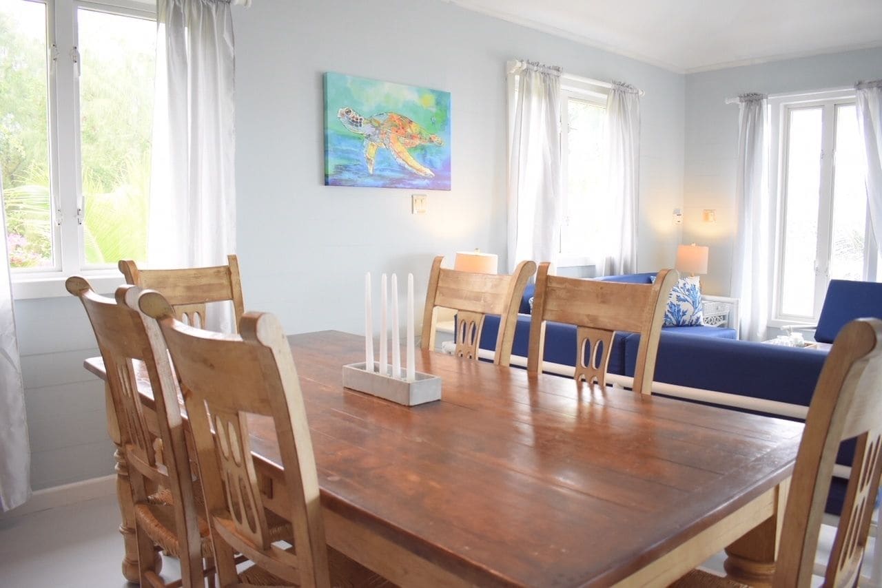 A dining area with a wooden table and chairs, a blue sofa, and a painting of a sea turtle on the wall.