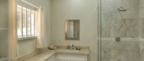 A bathroom with a glass shower enclosure, a sink with a mirror above it, and a window with curtains.
