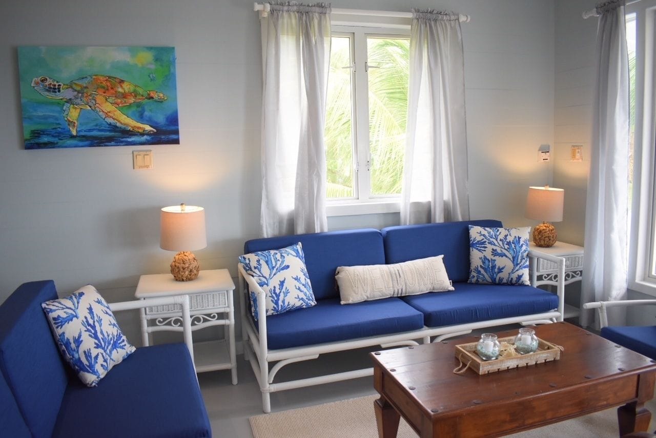 A room with a blue sofa, white side tables, a wooden coffee table, and a painting of a sea turtle.