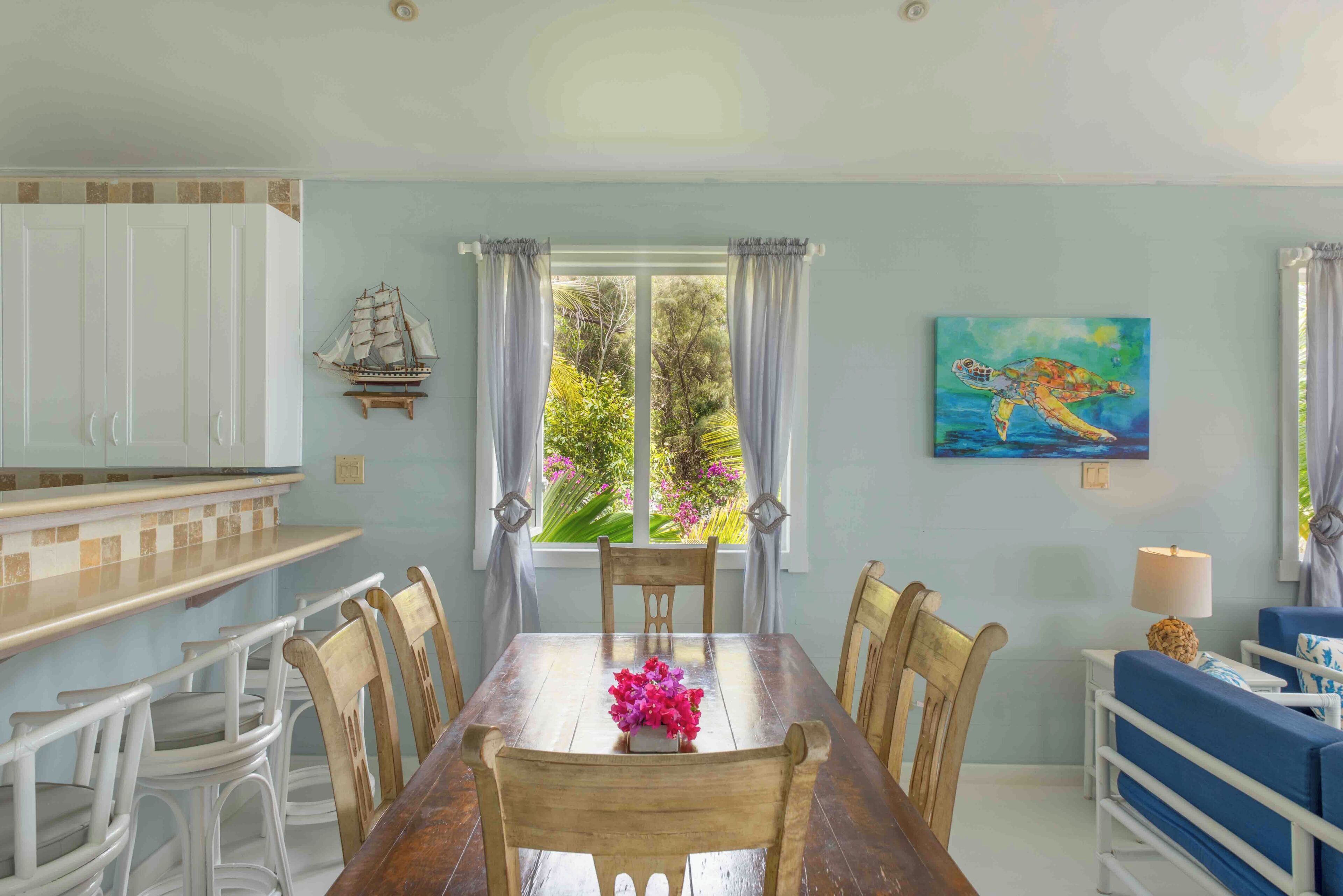 A dining area with a wooden table, white chairs, and a ship decoration on the wall.
