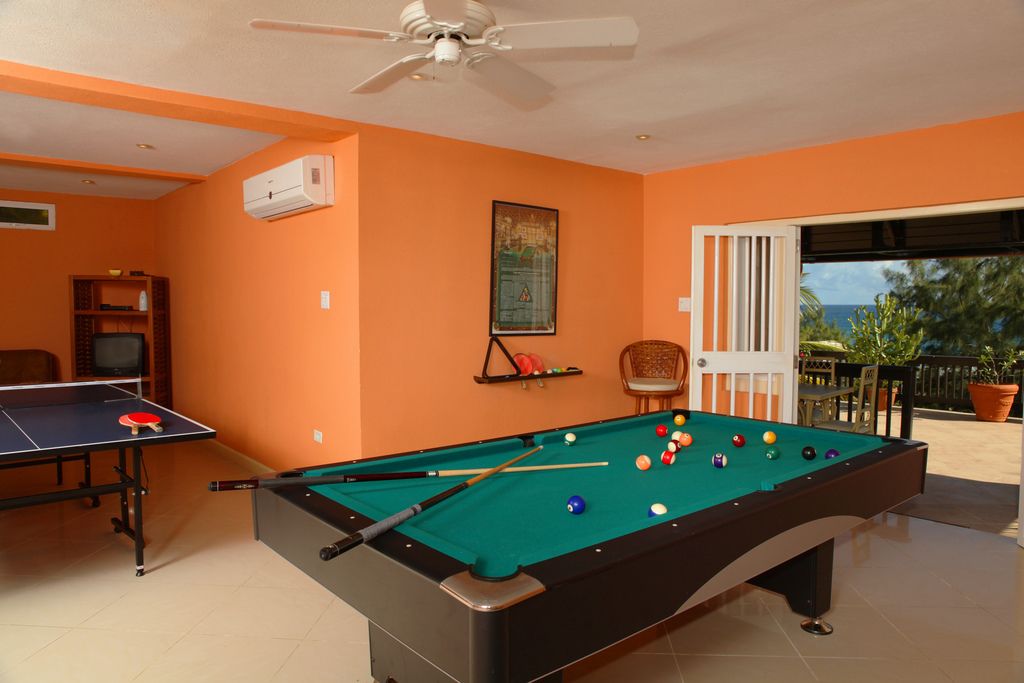 A pool table with balls, a ping pong table, and a ceiling fan in a room with orange walls.