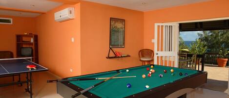A pool table with balls, a ping pong table, and a ceiling fan in a room with orange walls.