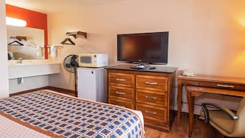 Quarto de hotel com cama, escrivaninha, televisão, micro-ondas, ventoinha e telefone.