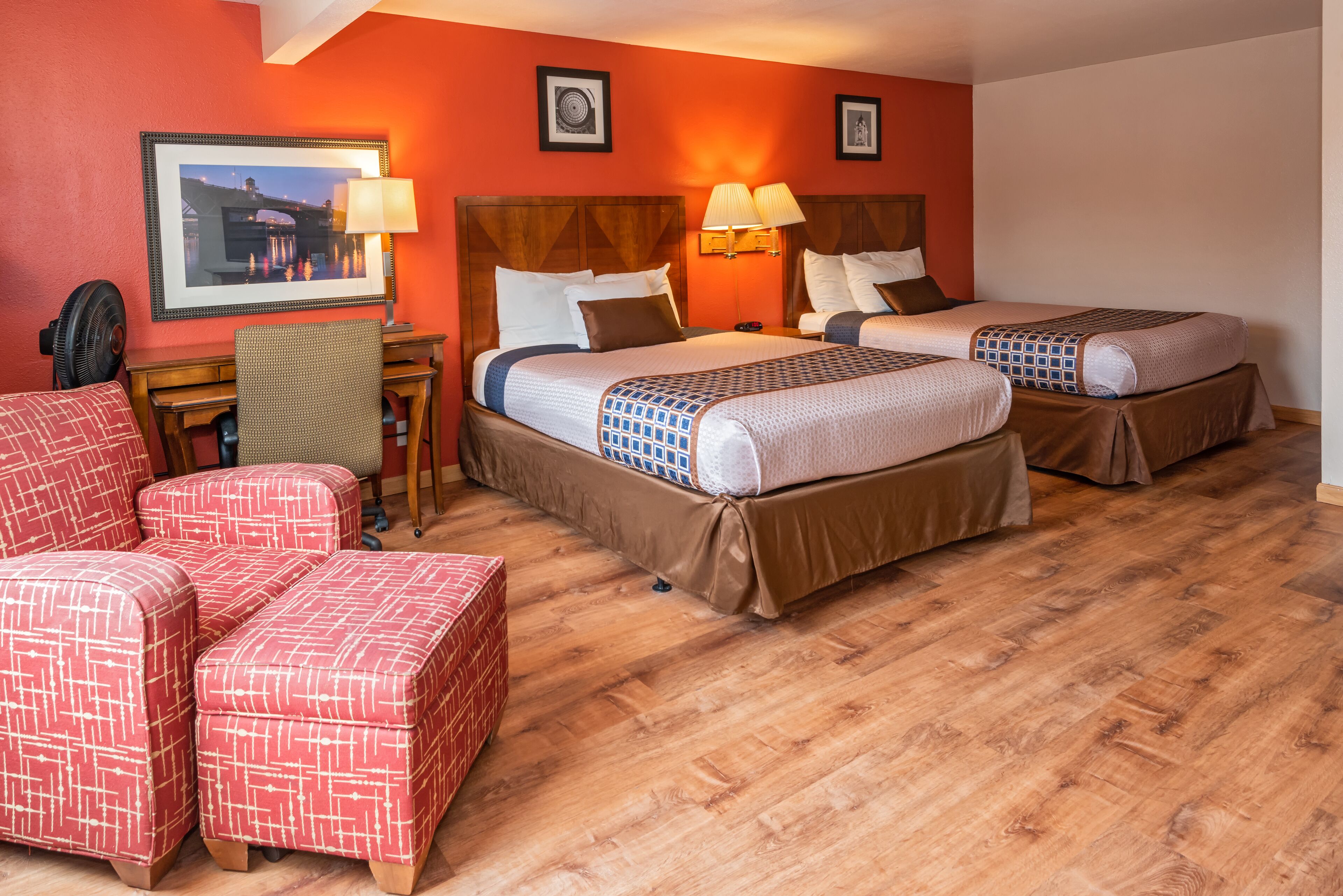 A hotel room with two beds, a desk, a chair, and a red couch.