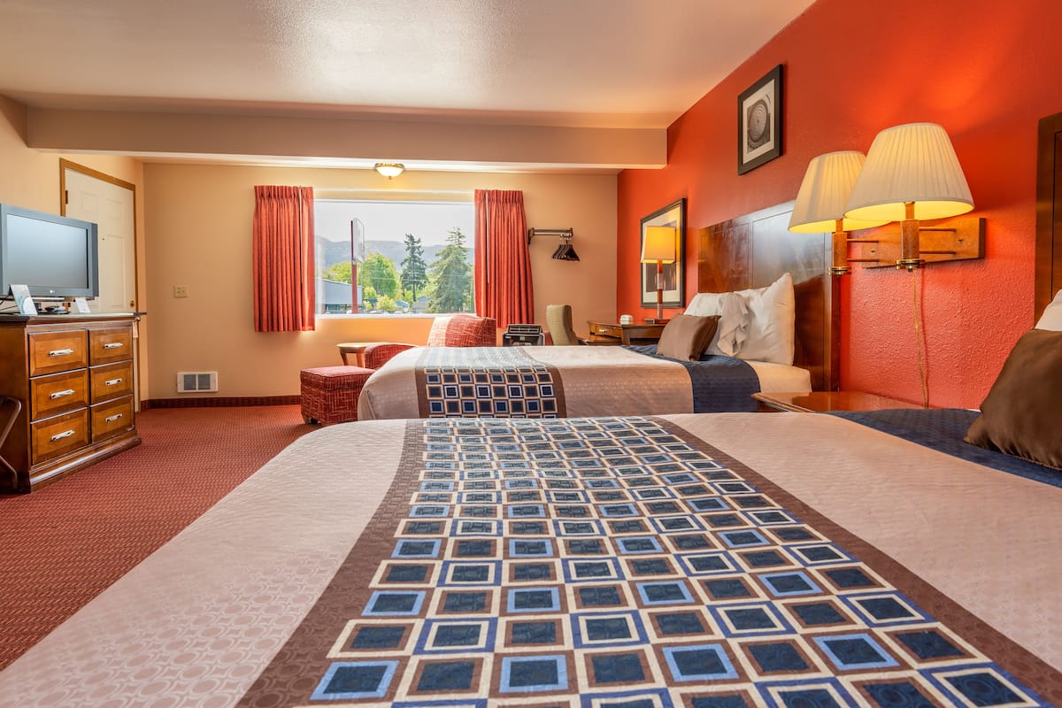 A hotel room with two beds, a desk with a computer, a TV, and a window with curtains.