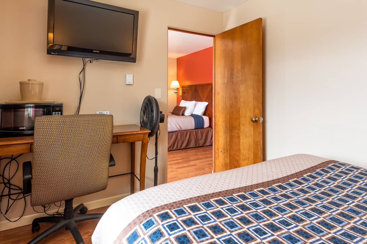 A hotel room with a bed, a desk with a computer, a chair, and a television on the wall.