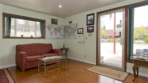 A living room with a red patterned sofa, a small table, a world map, and a door leading outside. - Flagstone Motel (Port Angeles)