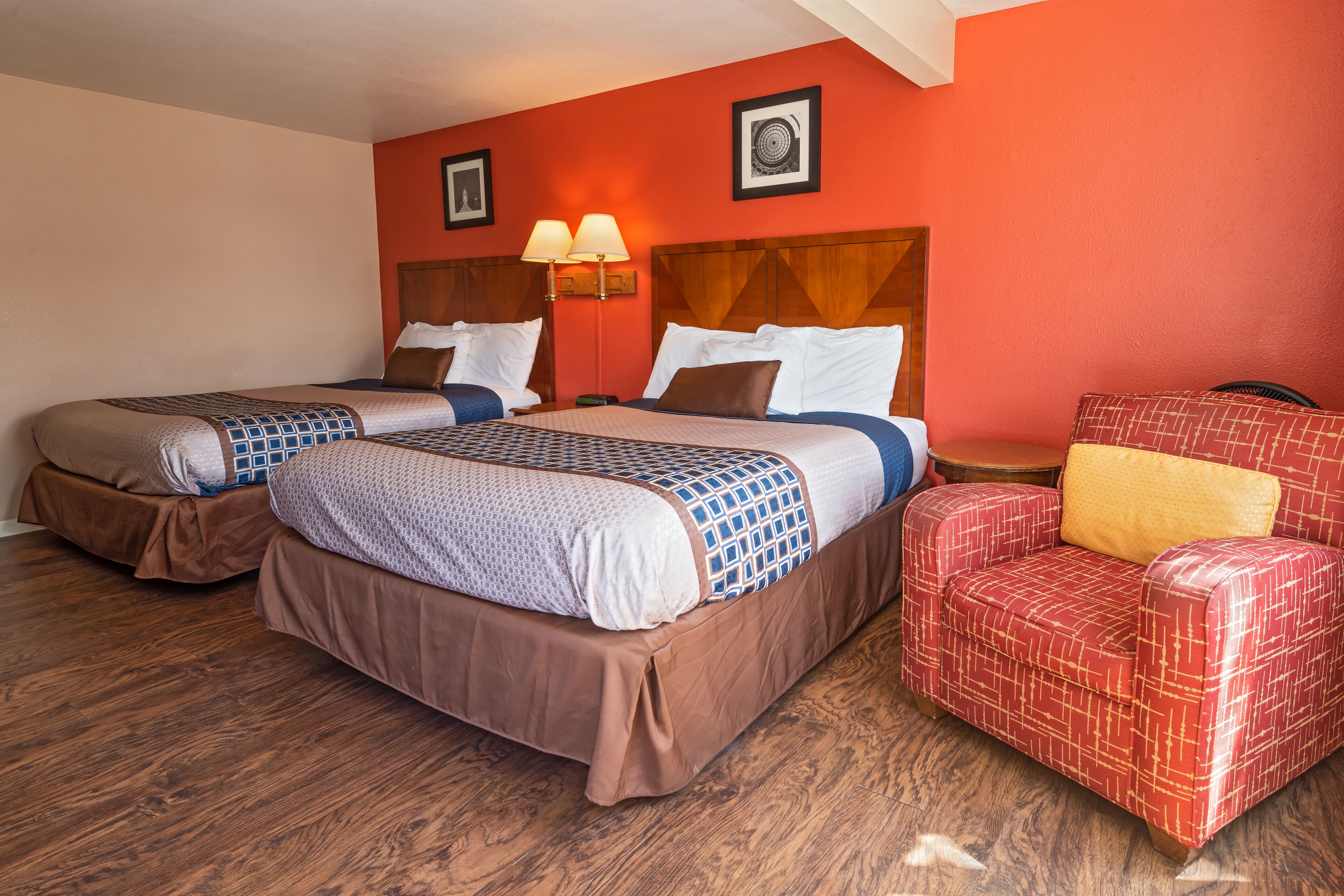 A hotel room with two beds, a red armchair, and a wooden headboard.
