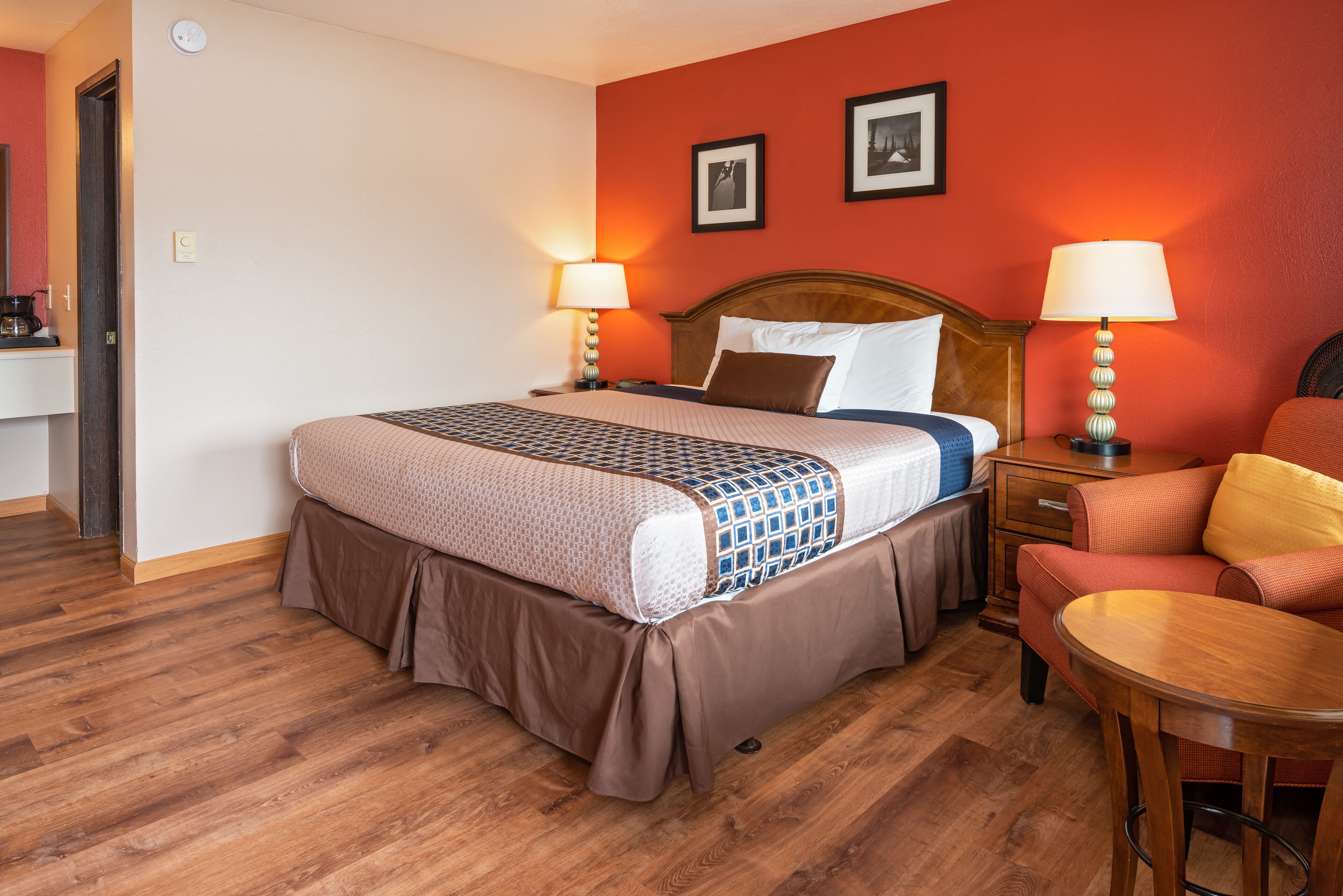 A hotel room with a large bed, two bedside lamps, a wooden nightstand, a red sofa, and a wooden table.
