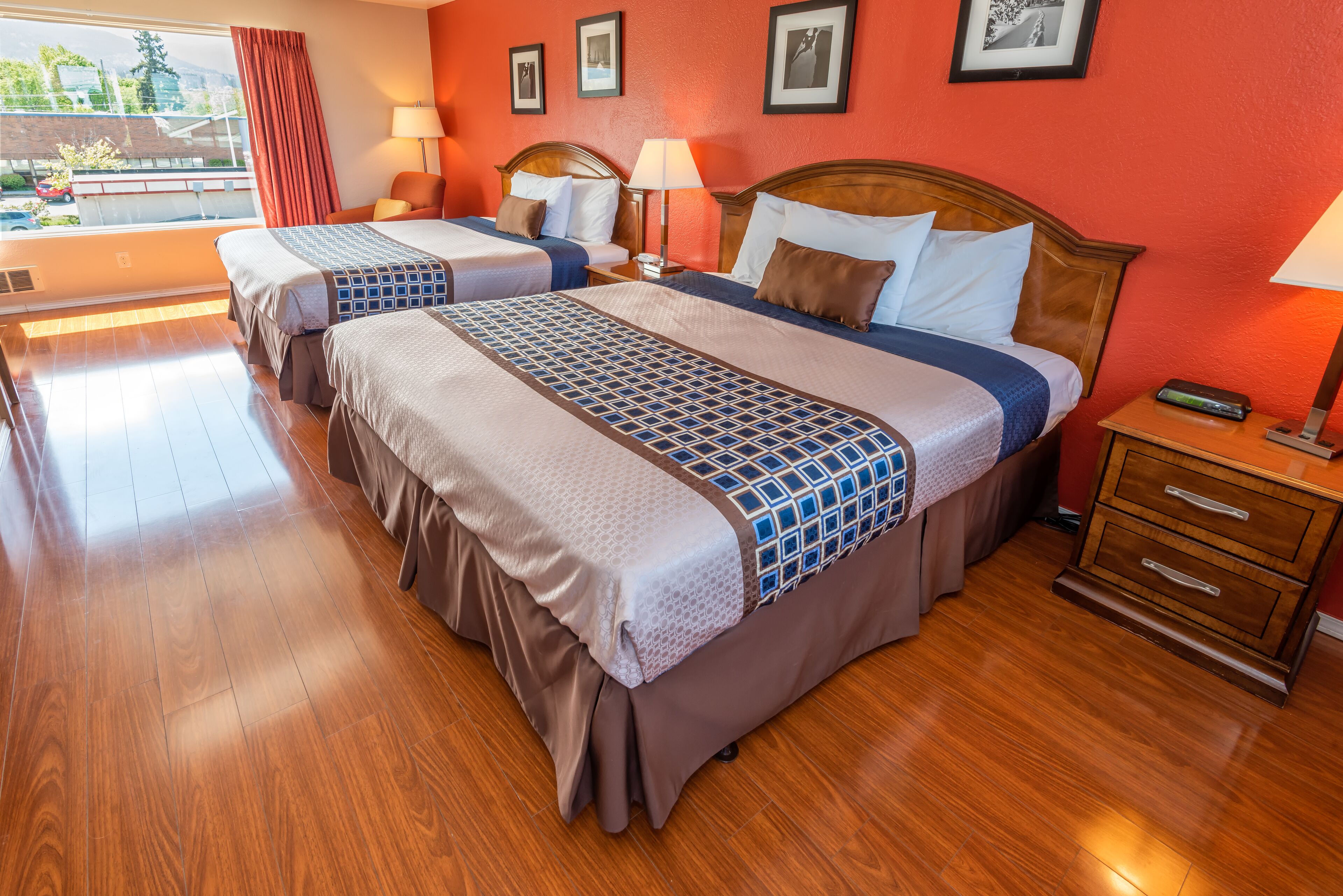 A hotel room with two beds, wooden flooring, and a view of the outdoors.