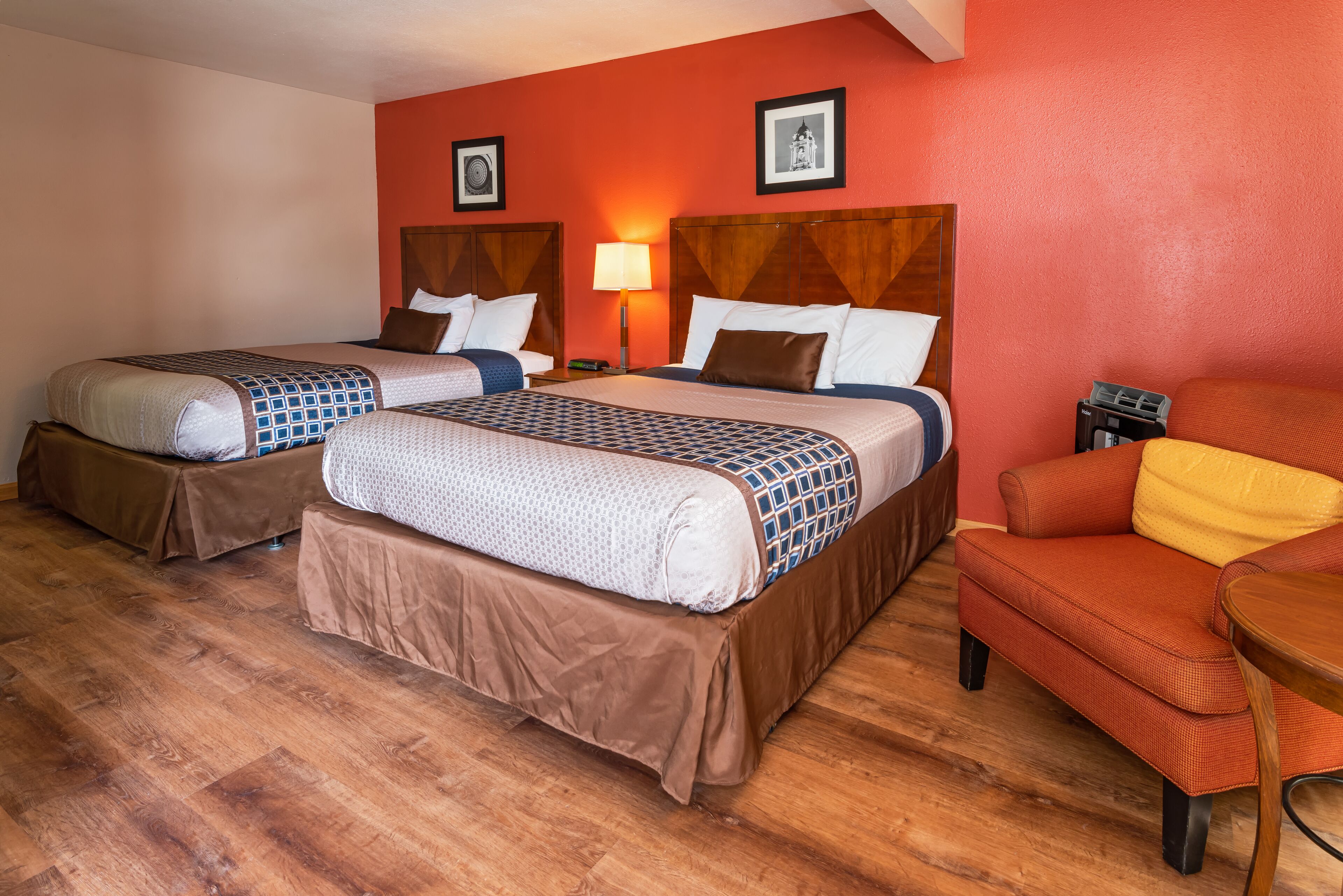 A hotel room with two beds, wooden flooring, and a red accent wall.