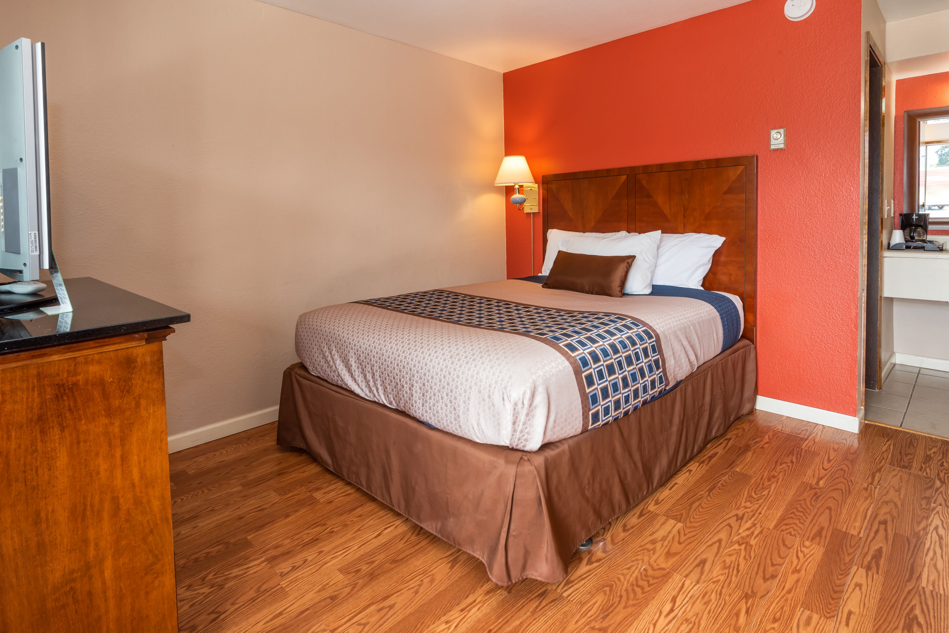 Habitación de hotel con un escritorio de madera, una cama con colcha estampada y una lámpara de pared.