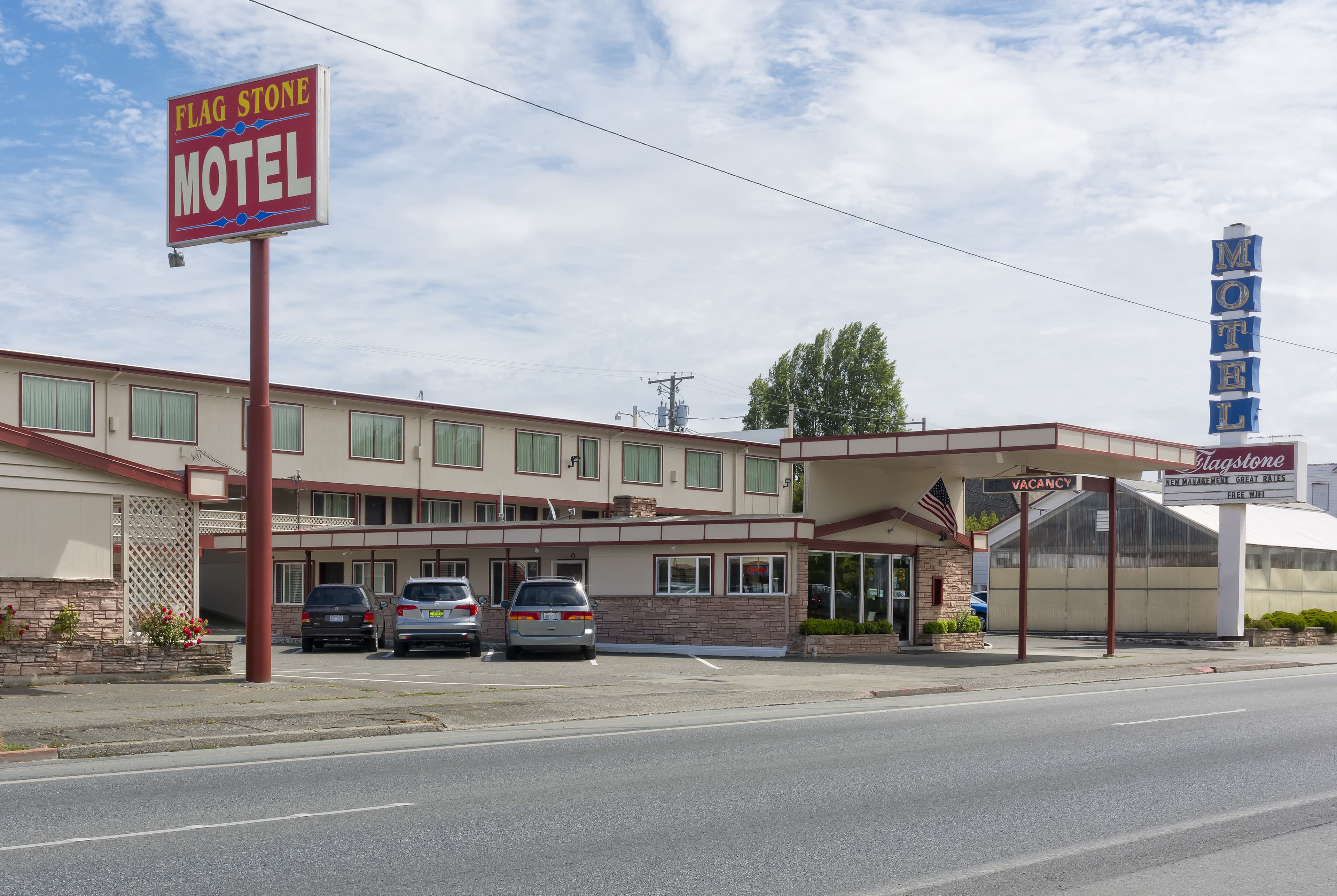 Un motel avec une enseigne, un parking rempli de voitures et un bâtiment doté d’un toit plat et de nombreuses fenêtres.