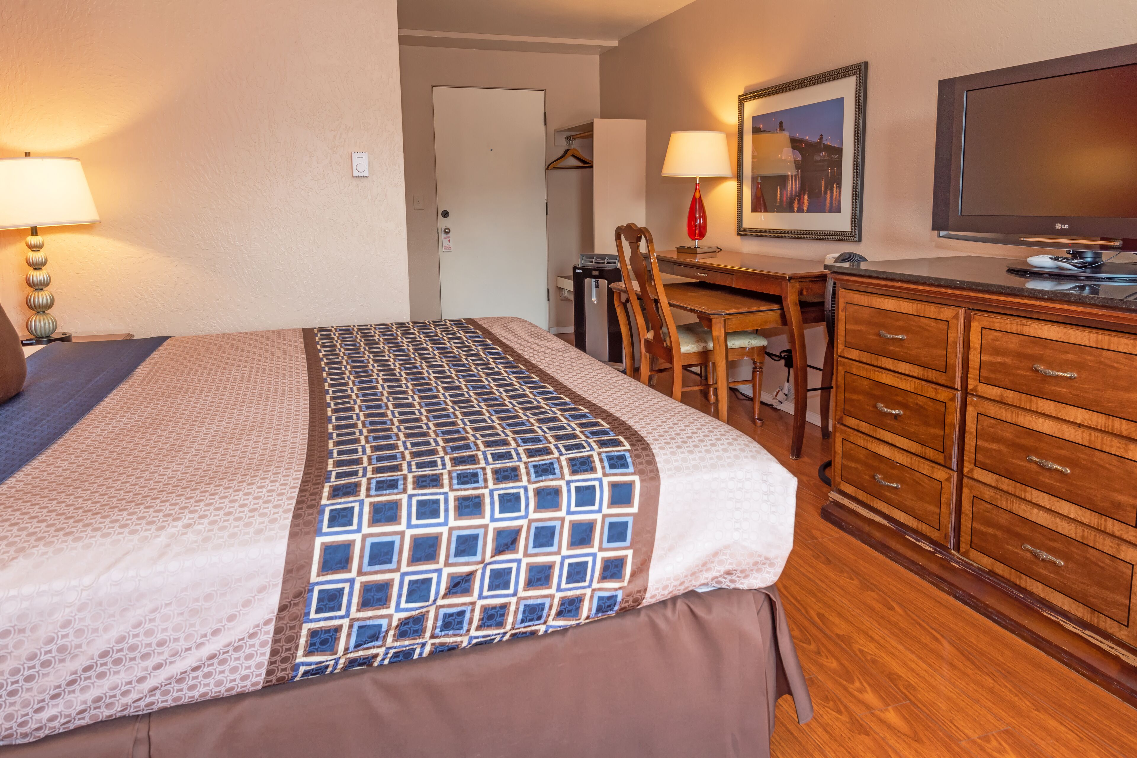 A hotel room with a bed, a desk, a chair, a TV, and a dresser.