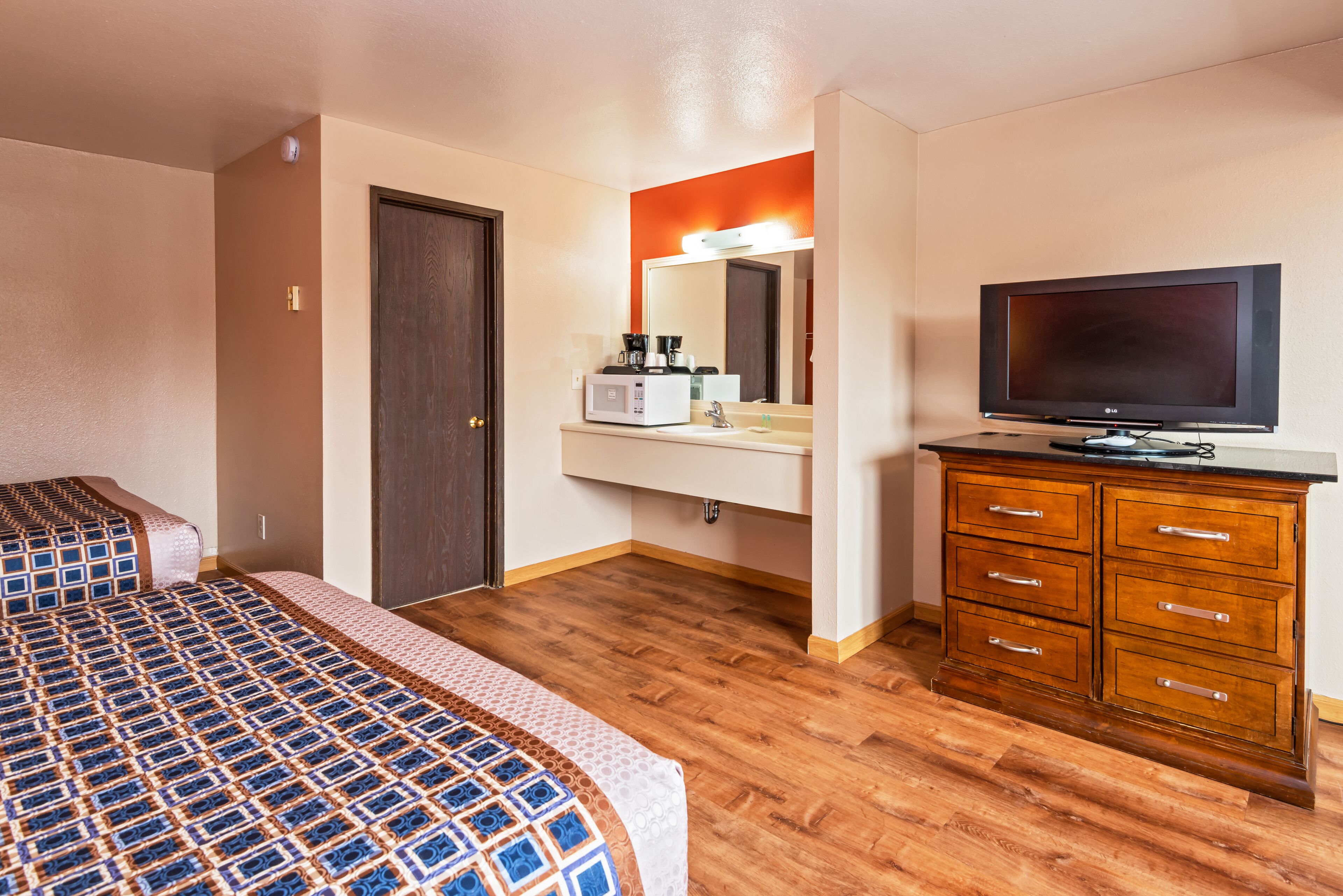A hotel room with a bed, a dresser, a television, and a bathroom vanity.
