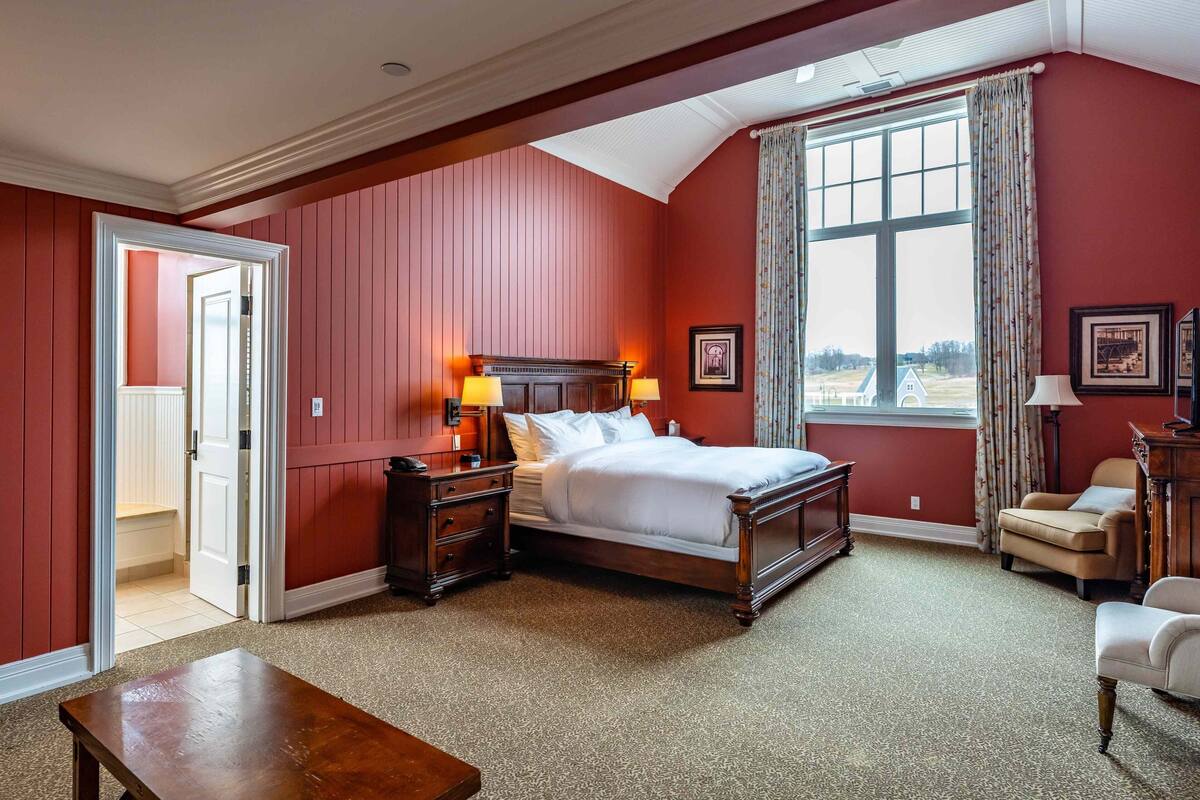 Une chambre avec un grand lit, deux tables de chevet avec des lampes, un fauteuil et une vue sur l’extérieur grâce à une grande fenêtre.