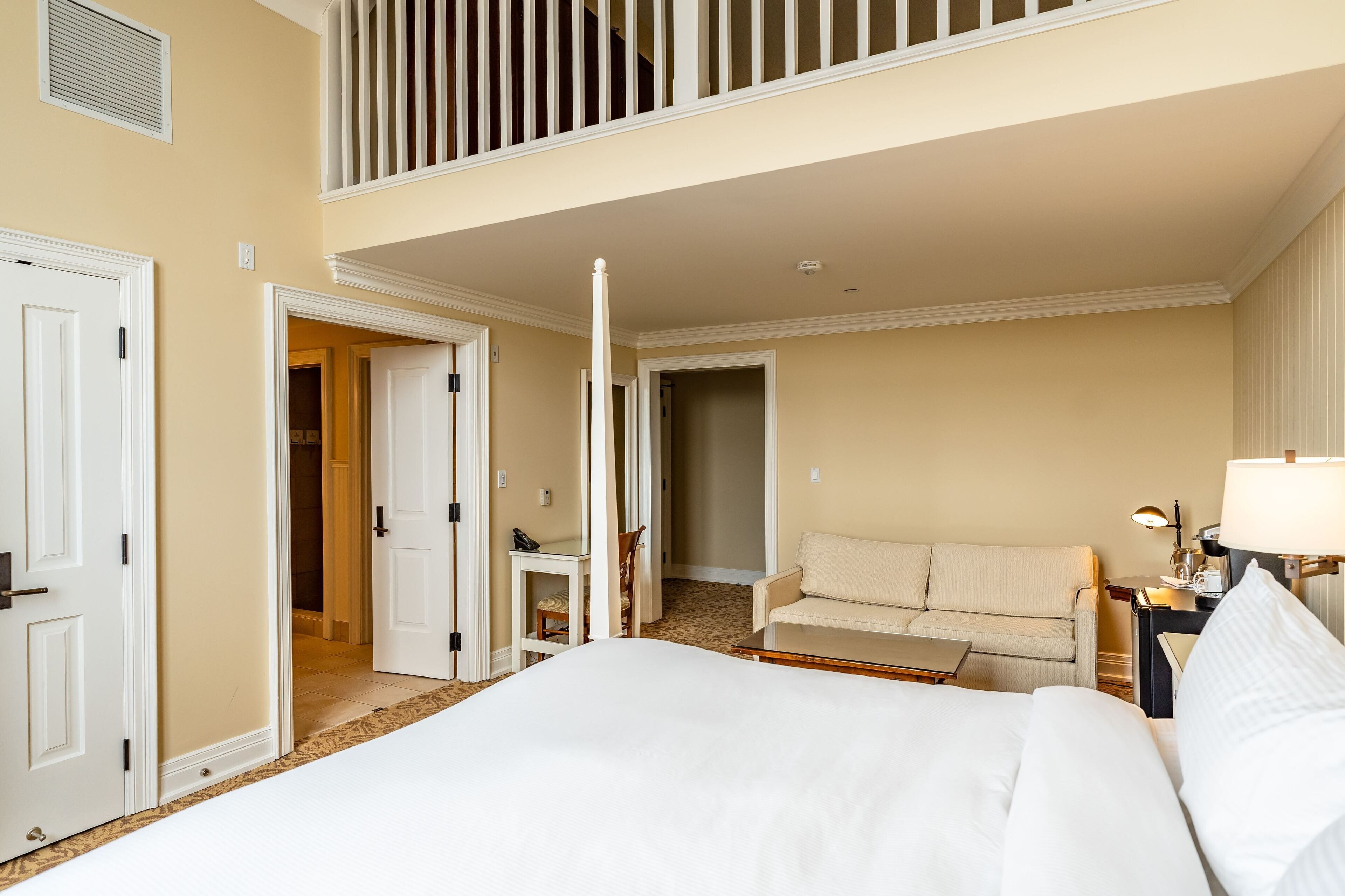 A hotel room with a large bed, a sofa, a desk, and a balcony.