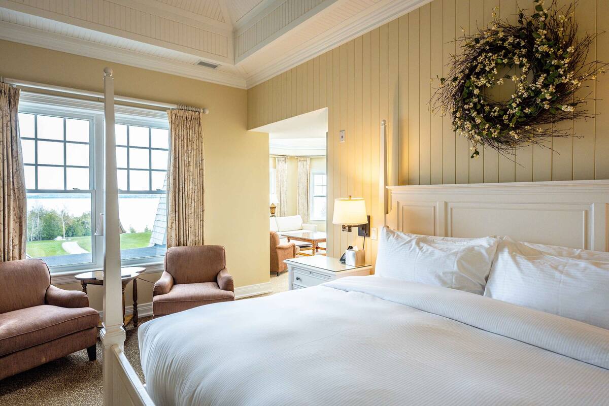 Une chambre d’hôtel avec un grand lit, deux fauteuils, une petite table, une lampe et une vue sur l’extérieur.