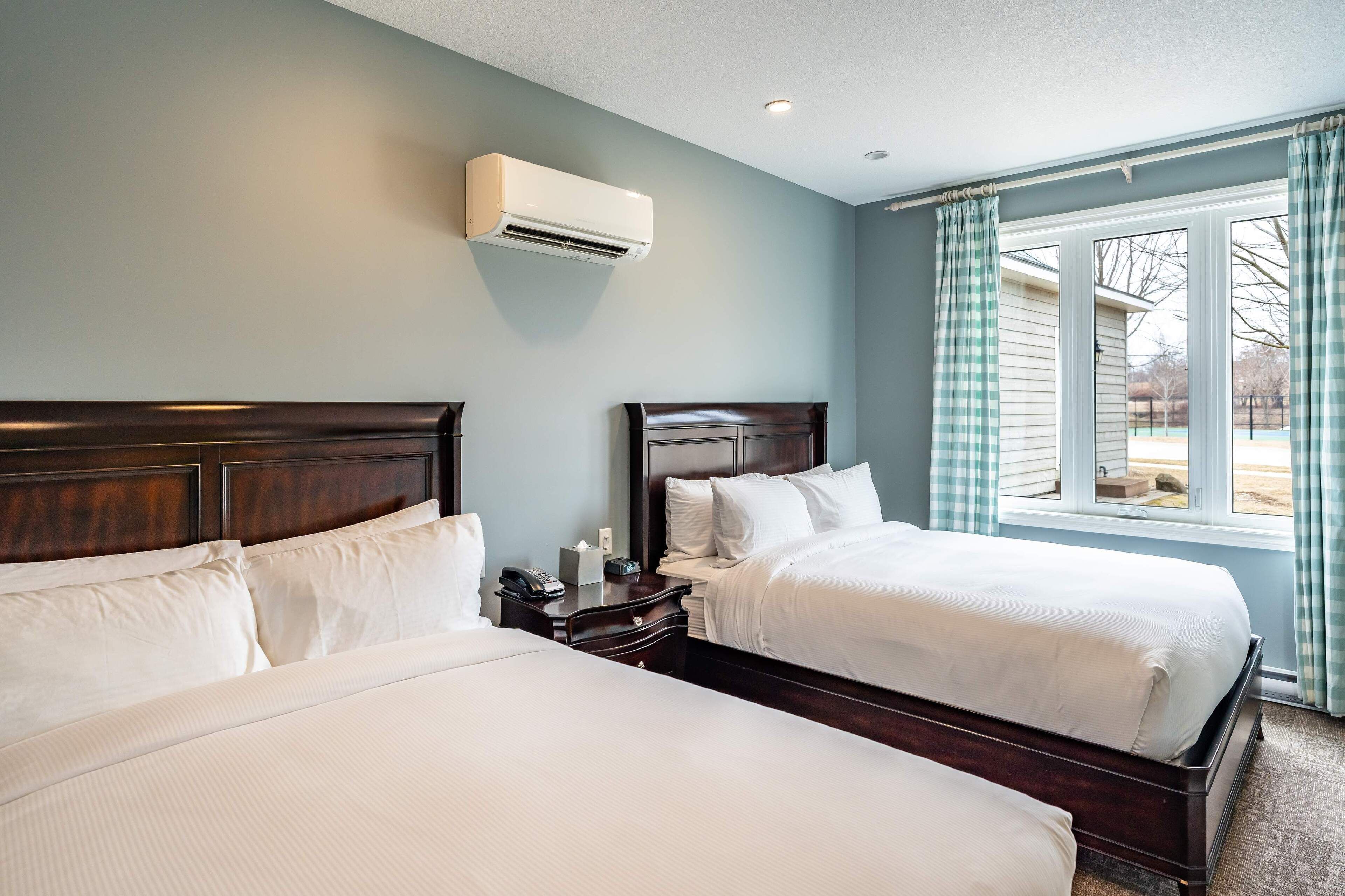 A hotel room with two beds, a nightstand, a phone, and an air conditioning unit.