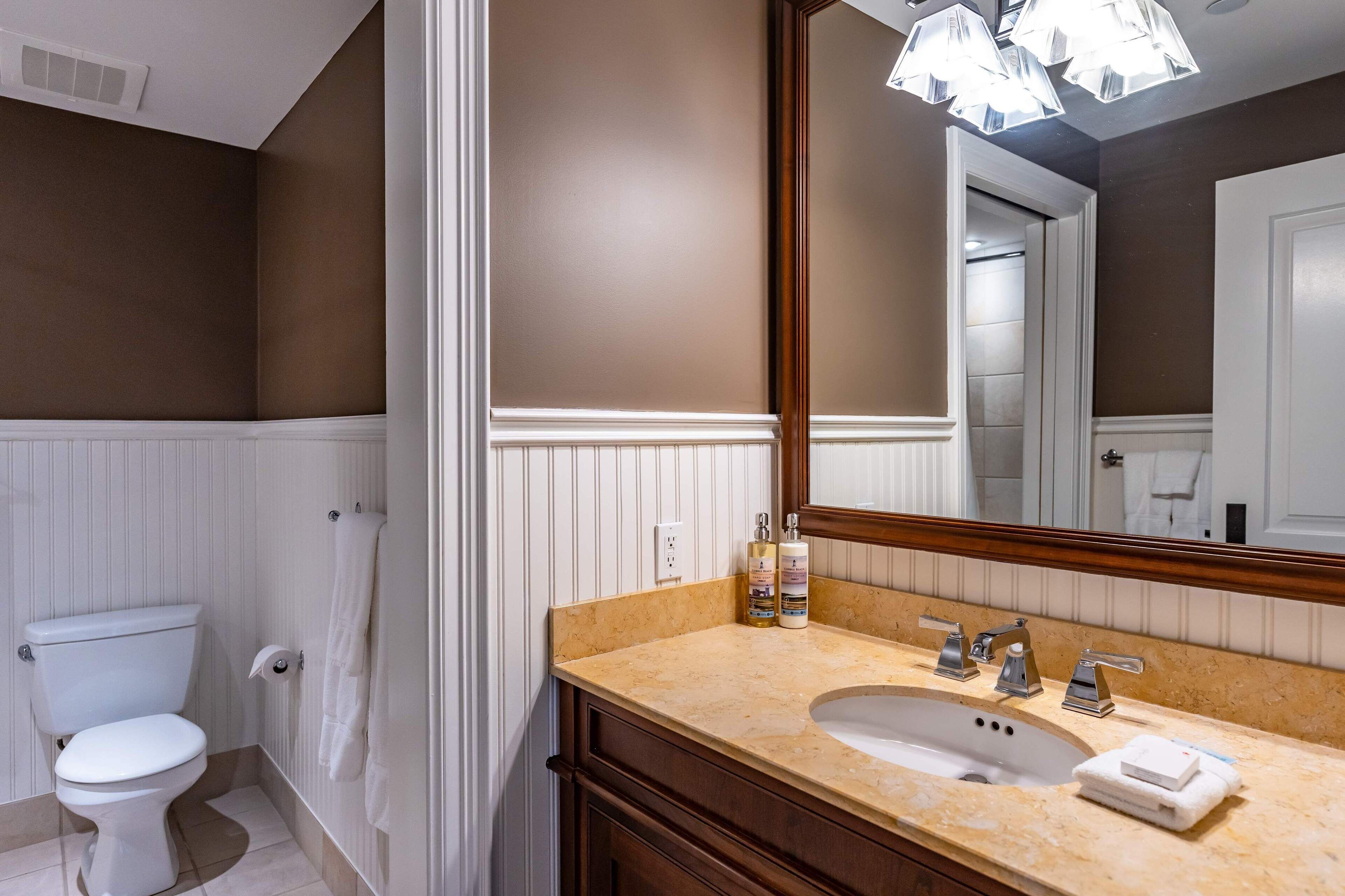 Un baño con inodoro blanco, lavabo color beige y un espejo grande.