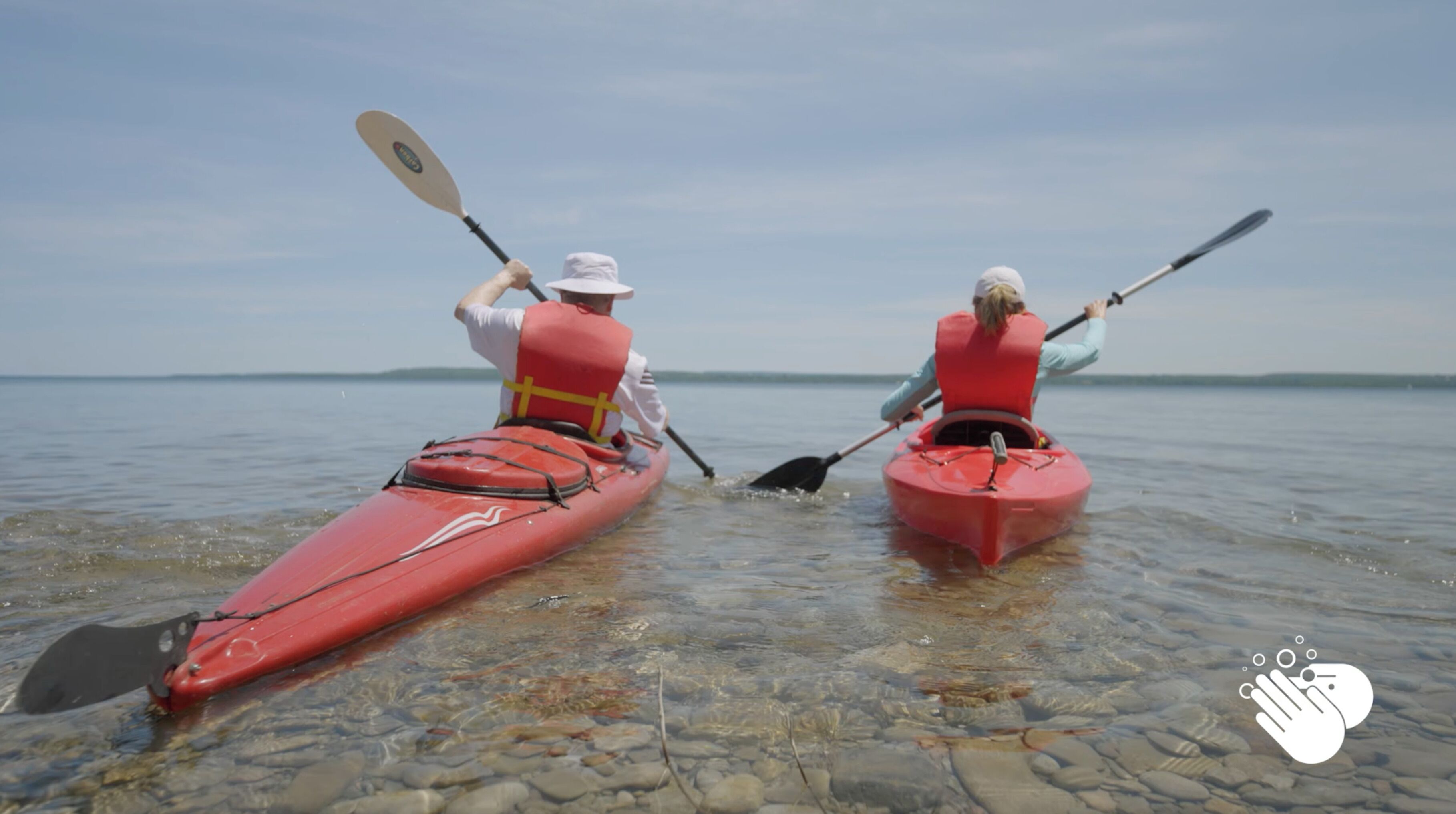 Dos personas remando en kayak sobre un lago tranquilo con aguas cristalinas y una orilla distante.