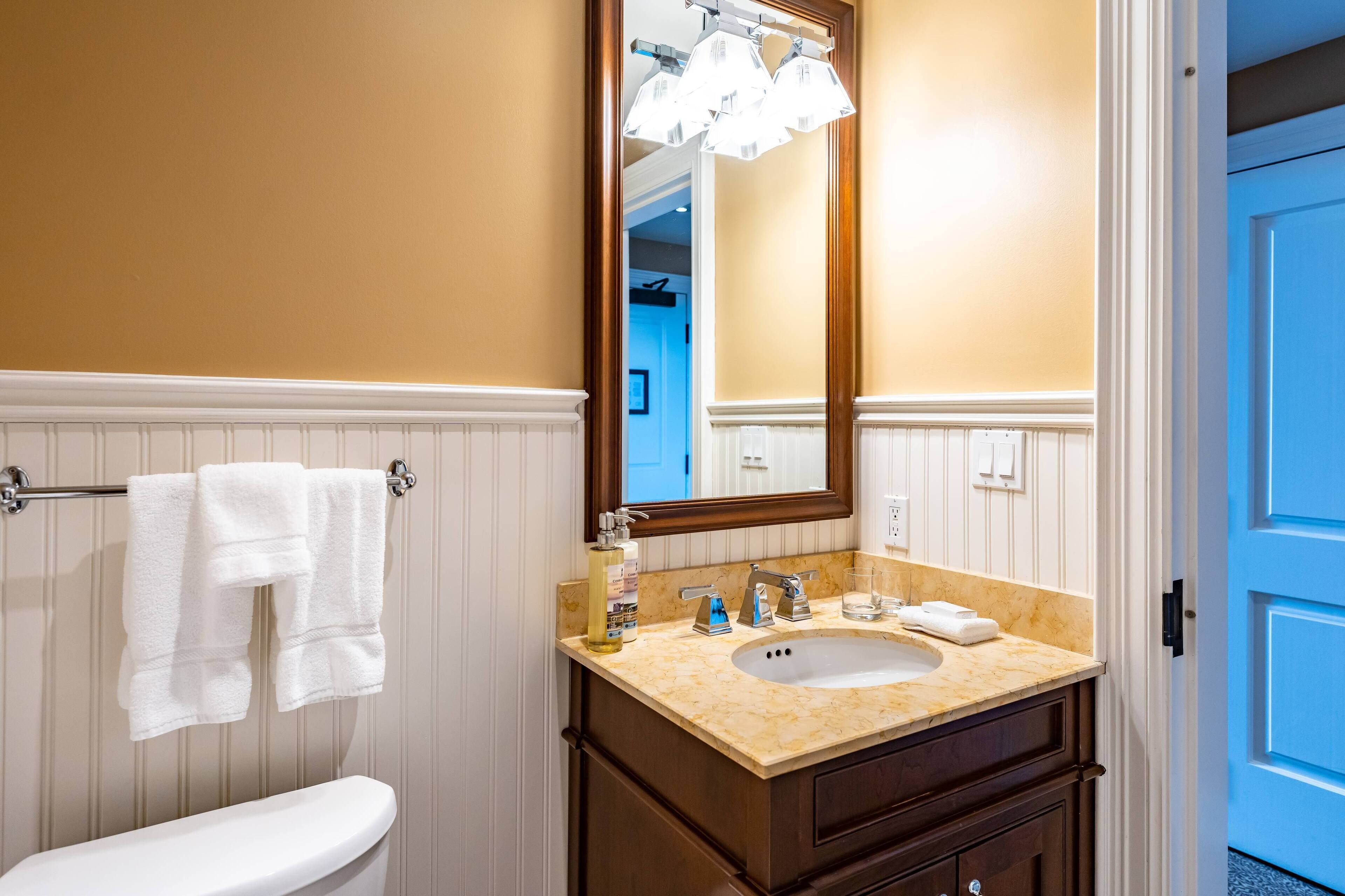 A bathroom with a white toilet, a beige sink with a mirror above it, and a towel rack with two towels.