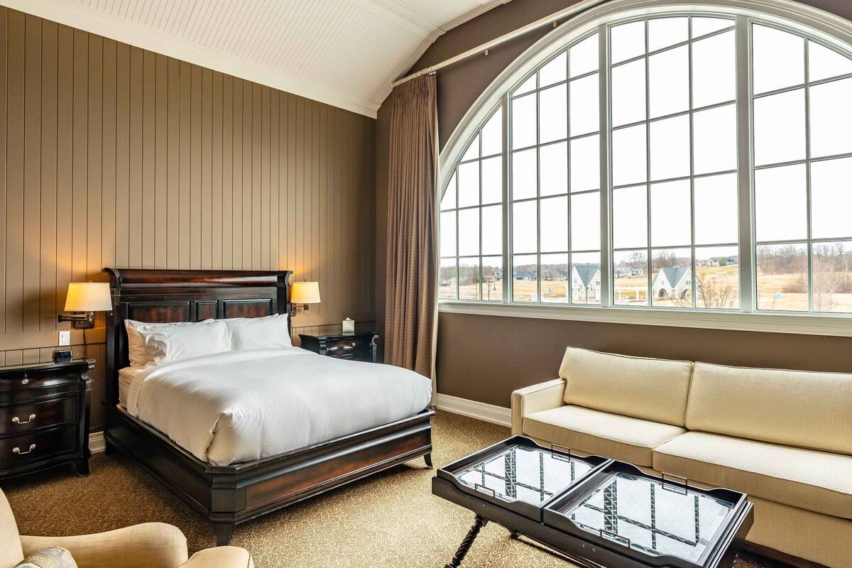 Une chambre d’hôtel avec un grand lit, un canapé, une table basse et une vue dégagée sur l’extérieur grâce à une grande fenêtre.