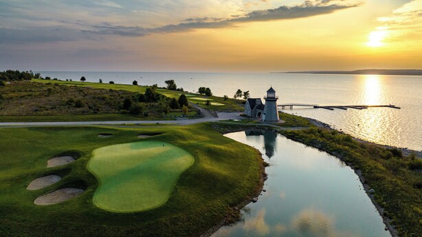 A golf course with bunkers, a lighthouse, and a body of water reflecting the sunset. - The Inn at Cobble Beach (Georgian Bluffs)