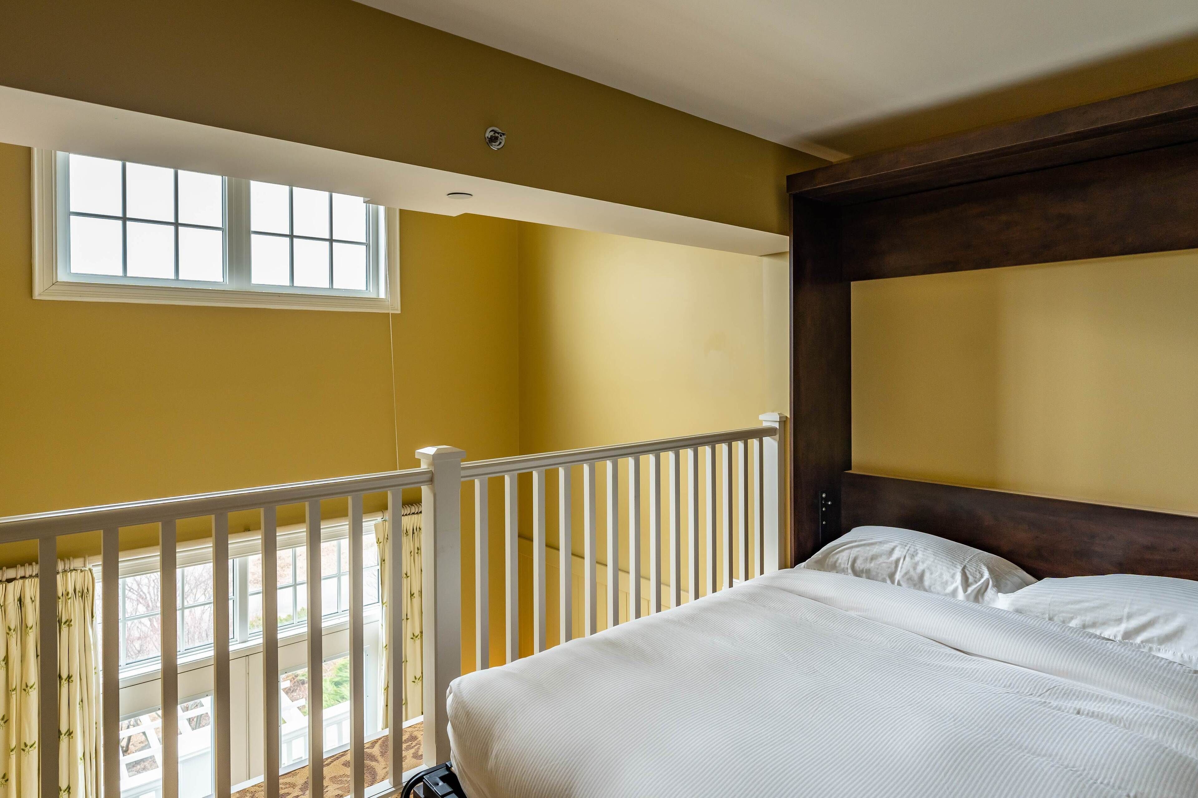 A bedroom with a bed, a window, and a balcony railing.