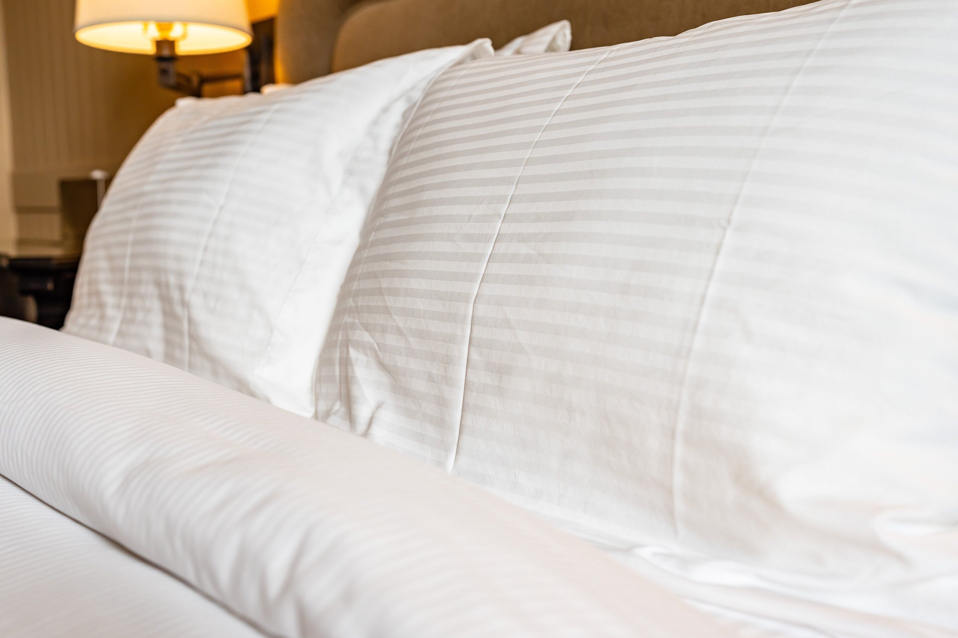 A neatly made bed with white linens and a striped pillow.