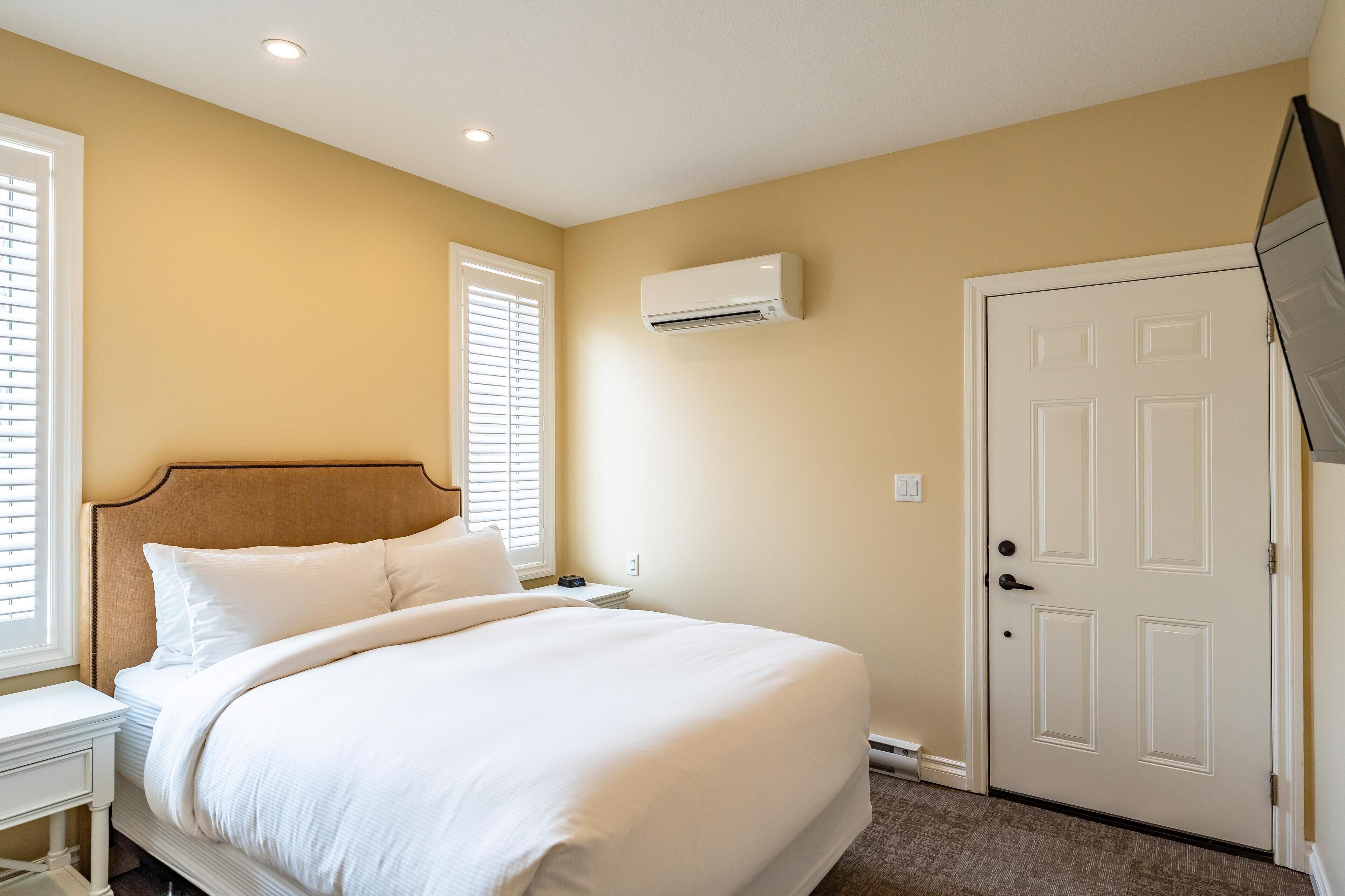Un dormitorio con cama, mesita de noche, aire acondicionado de pared y una puerta.