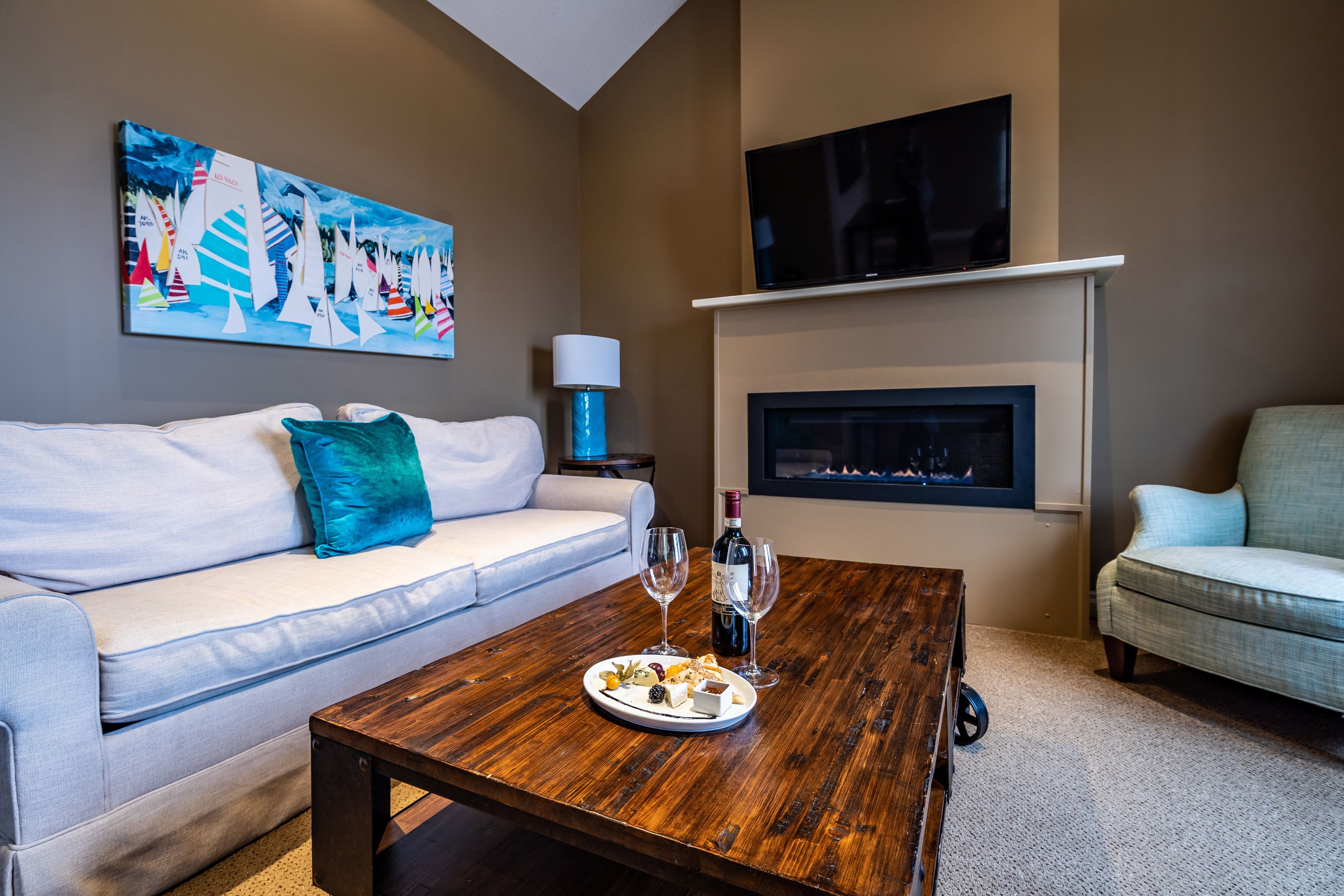 A living room with a sofa, a coffee table with a plate of food and wine glasses, a fireplace, and a TV mounted on the wall.