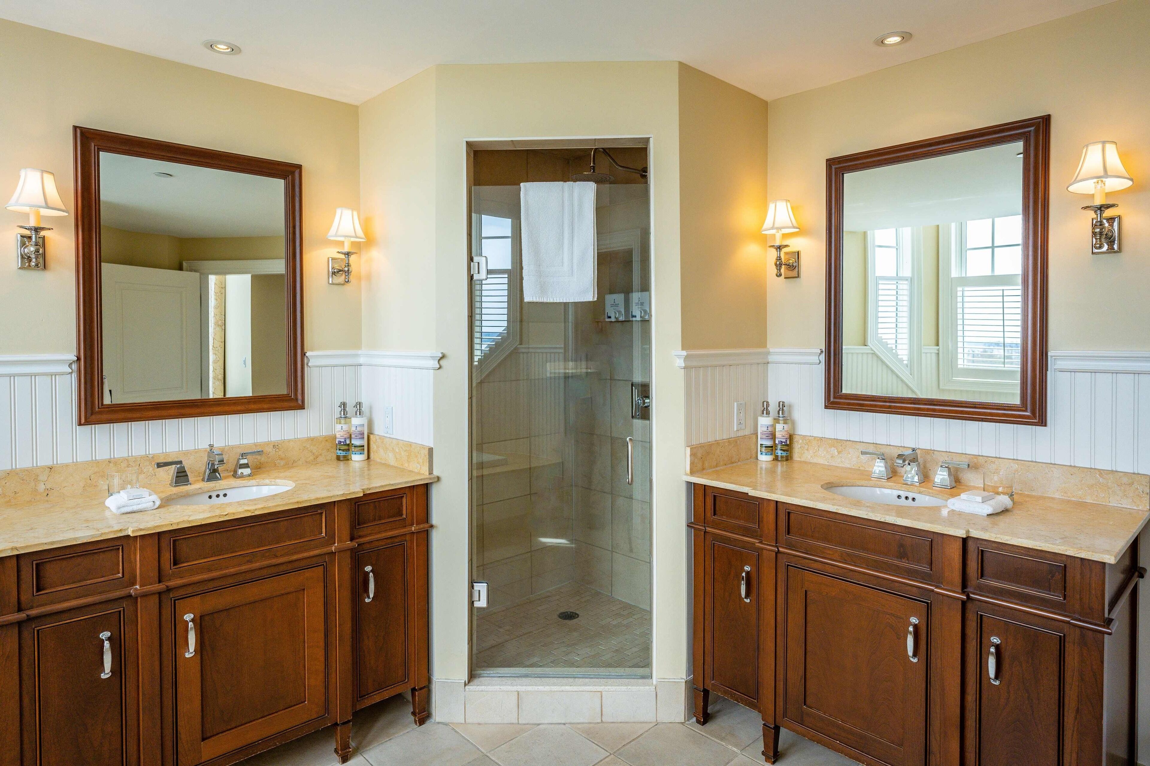 A bathroom with two sinks, wooden cabinets, and a glass shower enclosure.