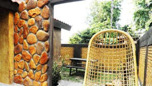 A stone wall, a wicker chair, a table, and a potted plant in an outdoor setting. - EFM Guest House (Ipoh)
