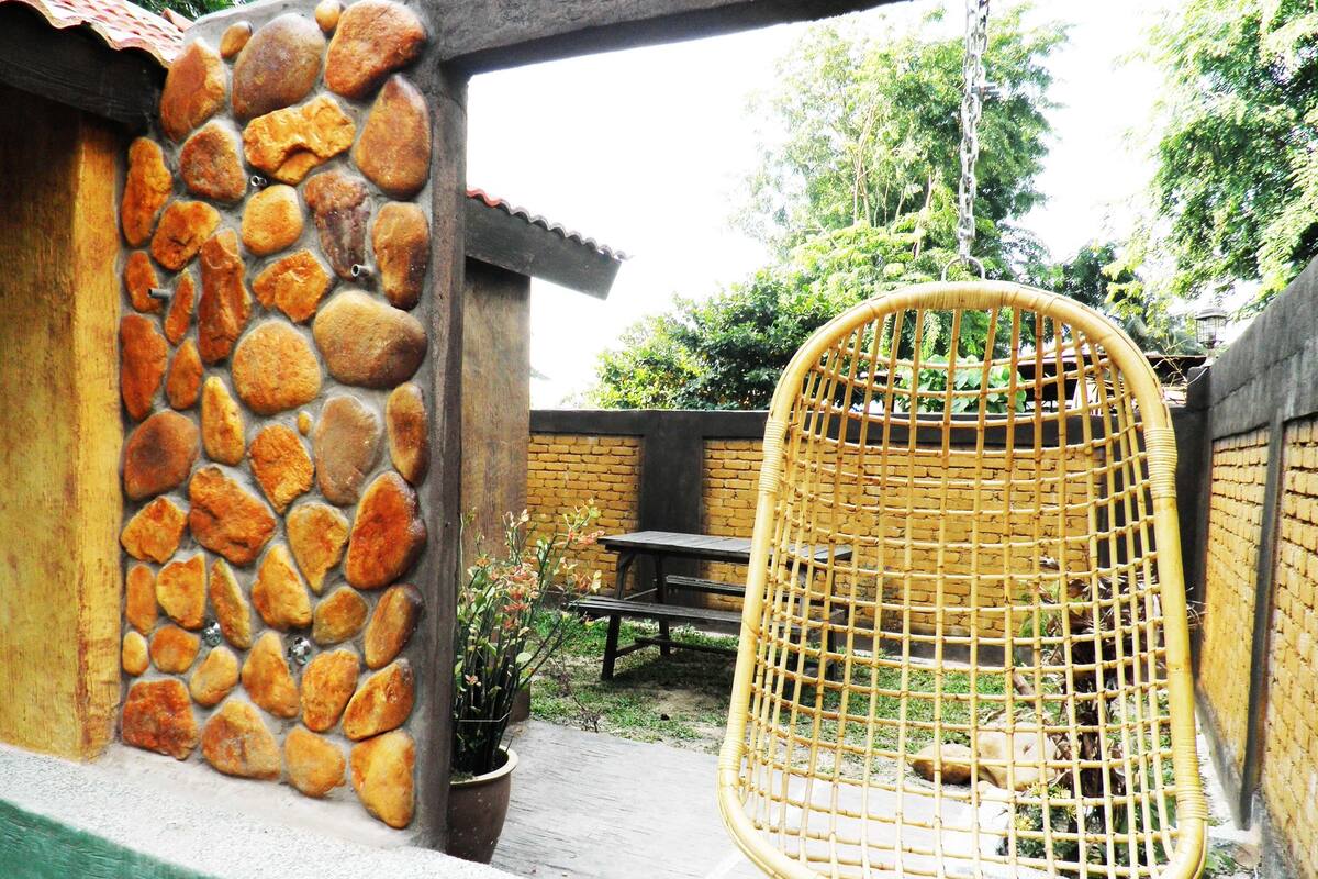 Un muro de piedra, una silla de mimbre, una mesa y una planta en maceta en un entorno al aire libre.