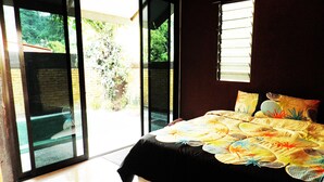 A bedroom with a large bed, a view of greenery through the window, and a sliding glass door leading outside. - EFM Guest House (Ipoh)