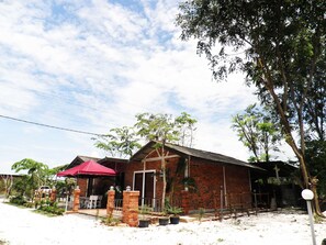 A brick building with a red roof, a covered patio area, and a small garden. - EFM Guest House (Ipoh)