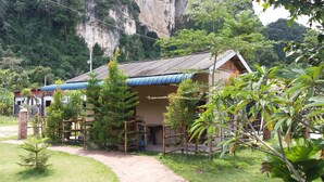 A rustic house with a corrugated metal roof, surrounded by lush greenery and a steep cliff in the background. - EFM Guest House (Ipoh)